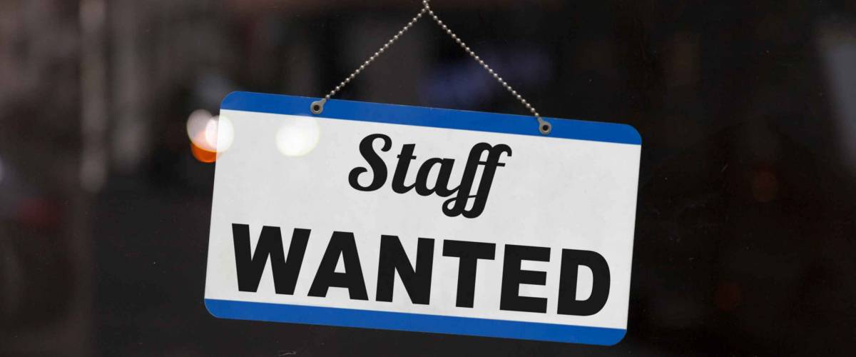 Close-up on a blue open sign in the window of a shop displaying the message: Staff wanted. hiring platforms for small business.