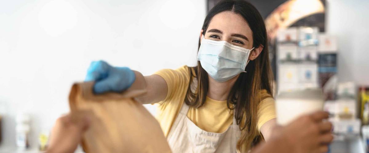 Bar owner working only with take away orders during corona virus outbreak - Young woman worker wearing face surgical mask giving takeout meal to customers - Healthcare and Food drink concept