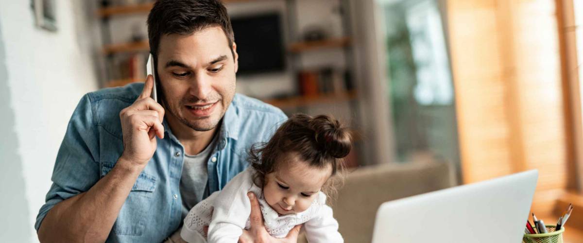 Young working father talking on the phone while babysitting his playful daughter at home.