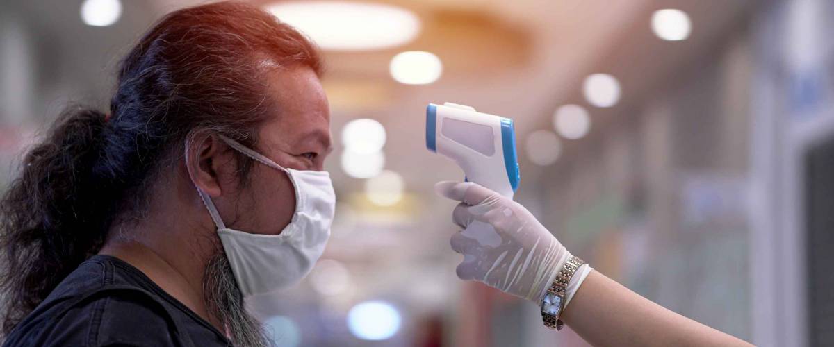 Coronavirus epidemic. Man having his temperature checked before entering the supermarket. Security procedures.
