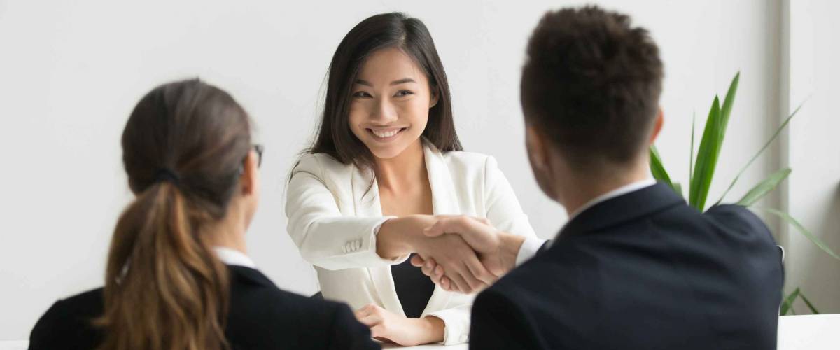 Happy millennial asian applicant getting hired shaking hand of hr employer