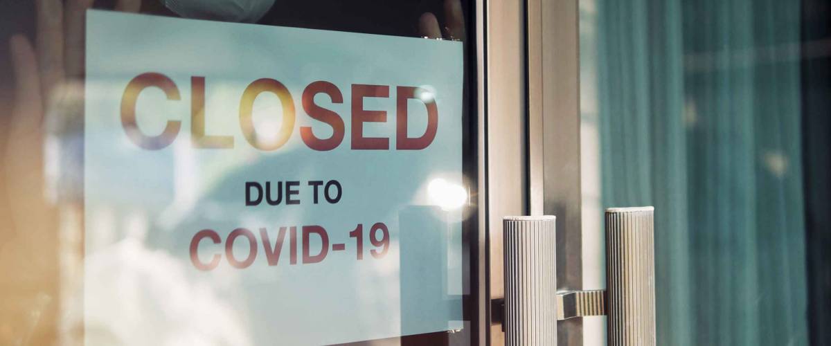 Unidentified person wearing mask hanging closed sign in background on front door.