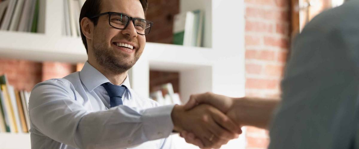 Smiling young Caucasian businessman shake hand of partner or colleague close deal after successful meeting in office.