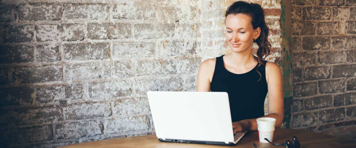 Casual young woman using laptop for distance job at coffee shop.