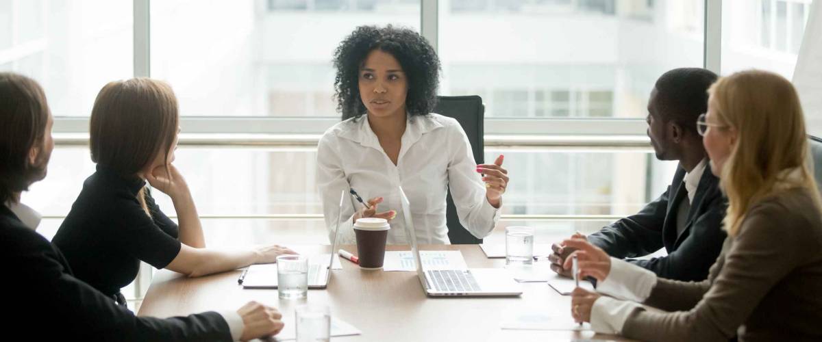 Black female boss leading corporate multiracial team meeting talking to diverse businesspeople