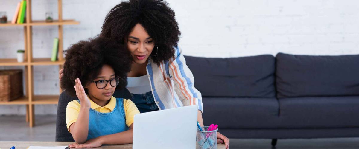 African american kid raising hand near laptop and mother at home