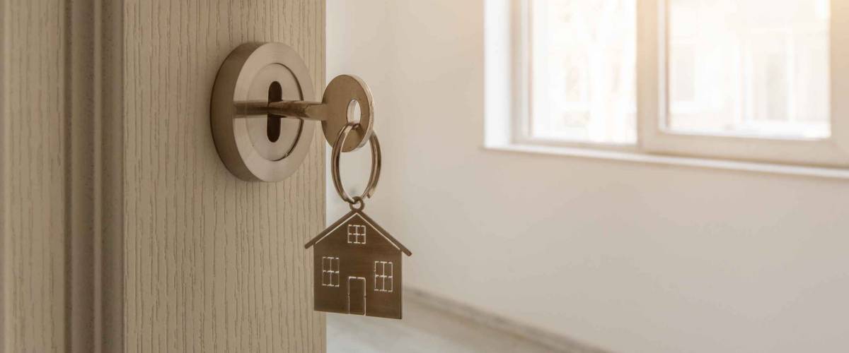 Open door to a new home with key and home shaped keychain. Mortgage, investment, real estate, property and new home concept