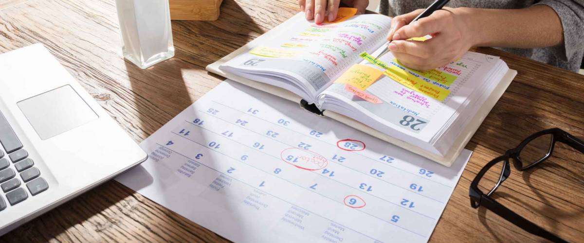 Close-up Of A Businesswoman Making Agenda On Personal Organizer At Workplace