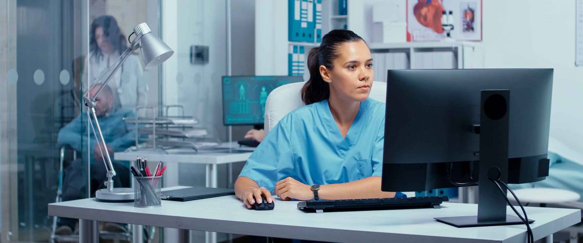 Nurse working on PC in modern private clinic with glass walls