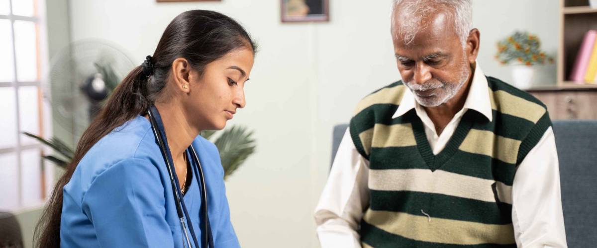 Young doctor or nurse writing prescription during home medical service or visit to senior man