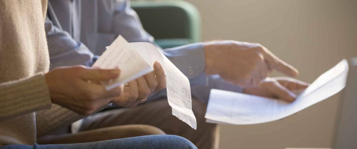 Elderly spouses sitting on couch at home planning budget, looking at medical bills.