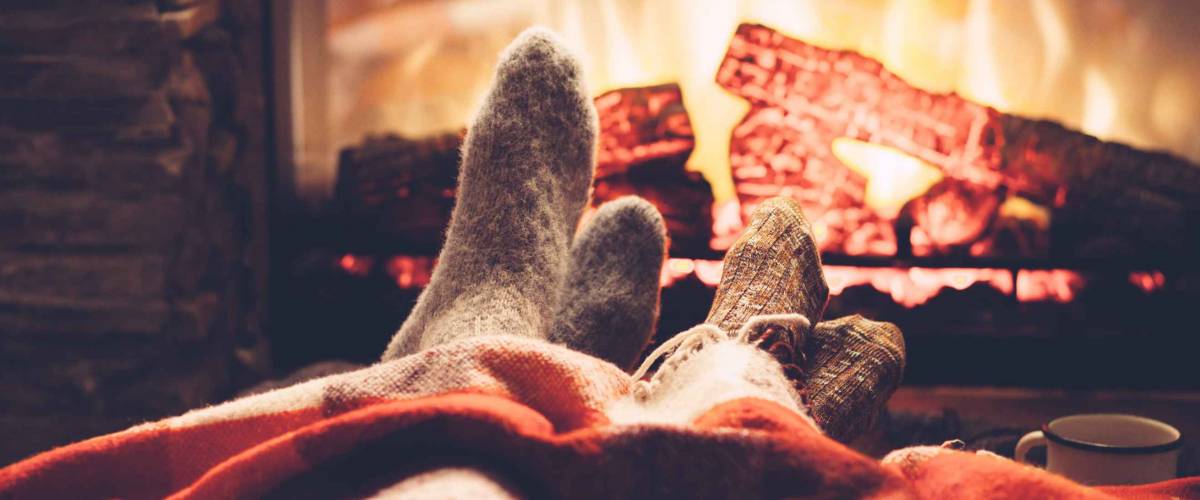 Cold fall or winter evening. People resting by the fire with blanket and tea. Closeup photo of feet in woolen socks. Cozy scene.
