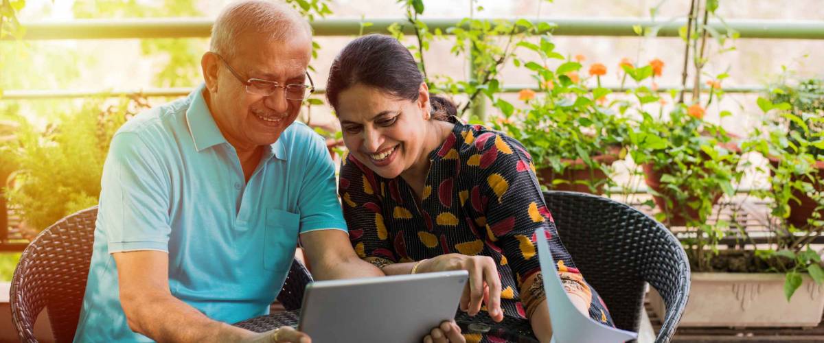Senior Indian/asian couple accounting, doing home finance and checking bills with laptop, calculator and money while sitting on sofa/couch or dining table at home