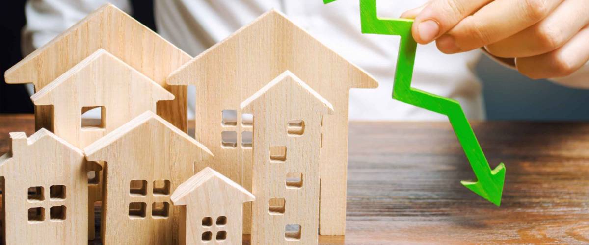 Analyst holds down arrow near the wooden houses. Concept of falling mortgage rates.