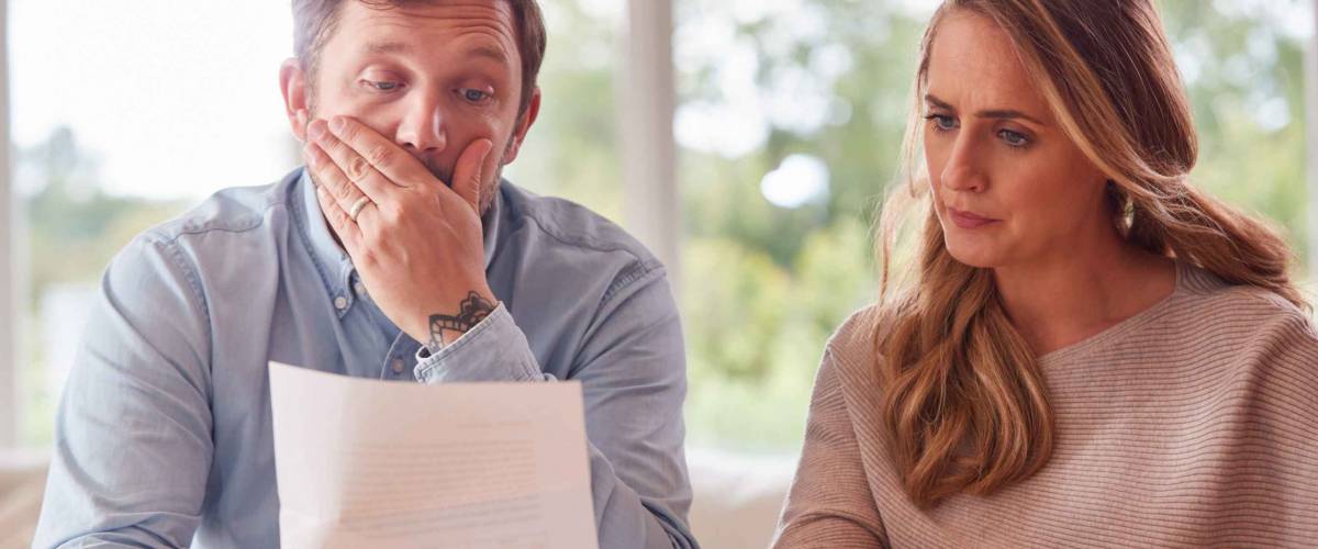 Worried Couple With Bills And Digital Tablet Sitting At Table At Home Reviewing Domestic Finances