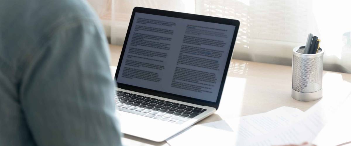 Close up young businessman working on research project, checking documents, holding paper sheet, looking at laptop screen, student writing diploma, essay, sitting at work desk, home office