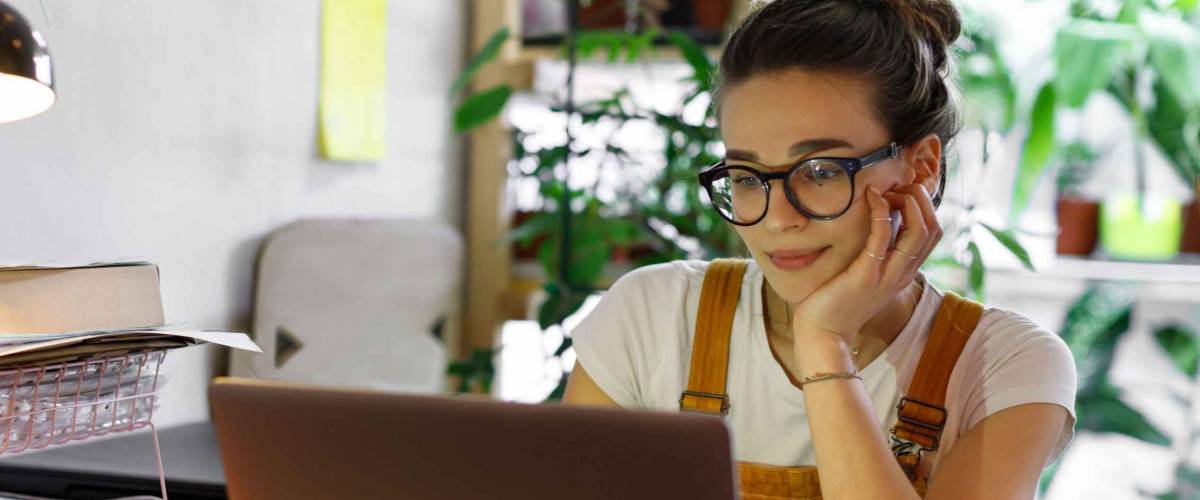 Young female gardener in glasses using laptop looking for a student loan refinance.