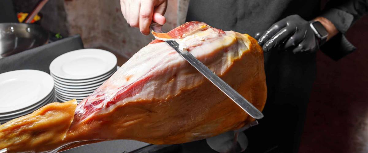 The cook cuts ham into thin slices with a knife. The concept of restaurant service.