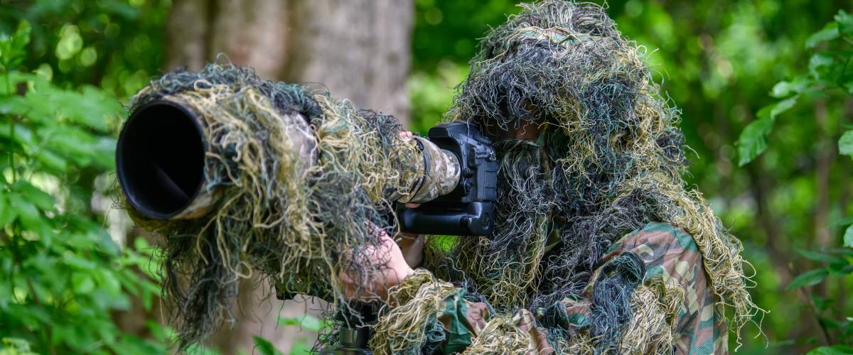 Wildlife photographer in the summer ghillie camouflage suit working in the wild