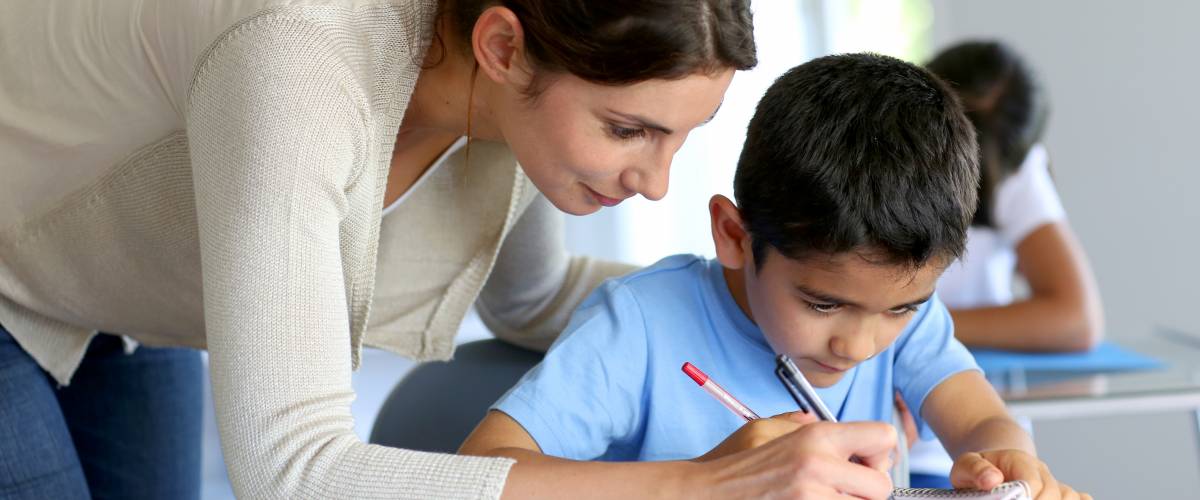 Teacher helping young boy with writing lesson