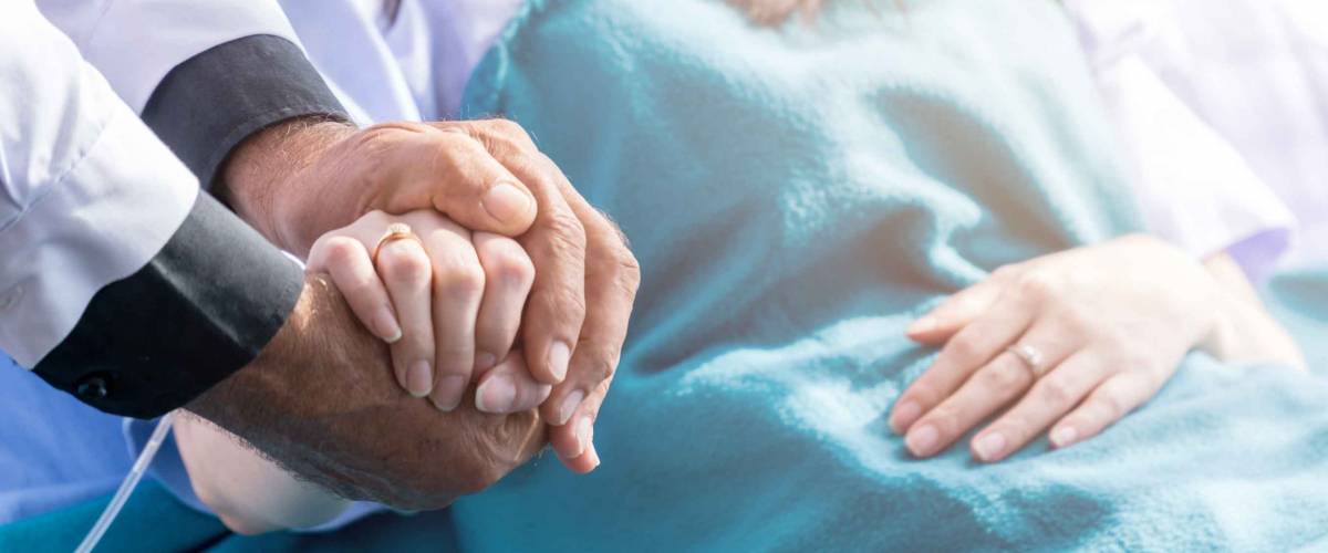 Male doctor holding female patient hand on the hospital bed.