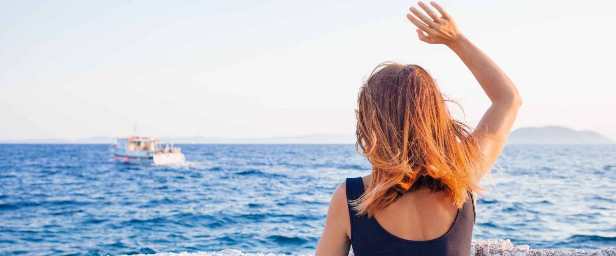 Young woman waving to a boat from the pier