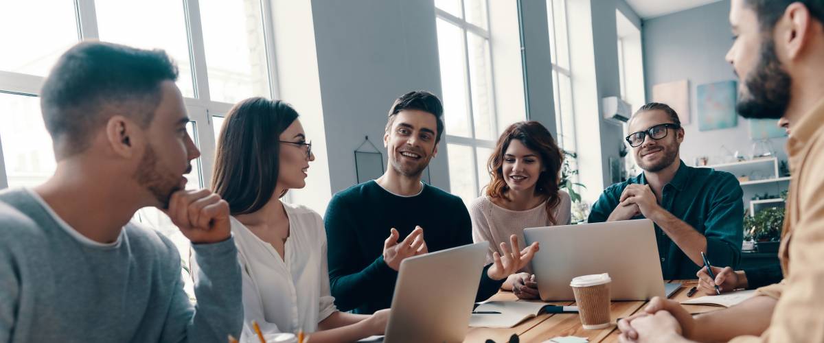 Group of young modern people in smart casual wear discussing something and smiling while working in the creative office
