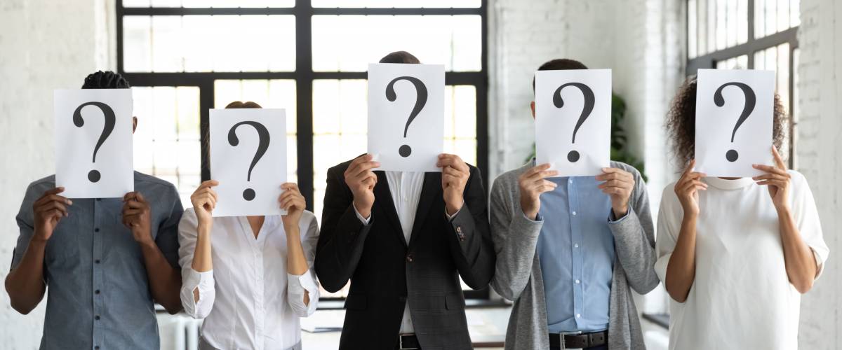Diverse business people hiding faces behind papers sheets with question marks, standing in row in office.