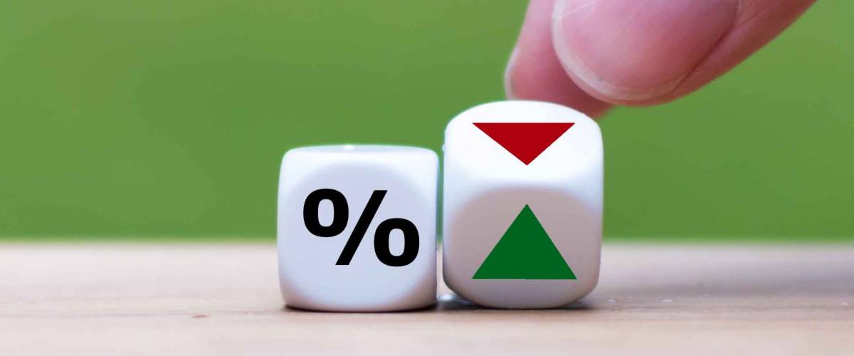 Hand is turning a dice and changes the direction of an arrow symbolizing that the interest rates are going down (or vice versa)