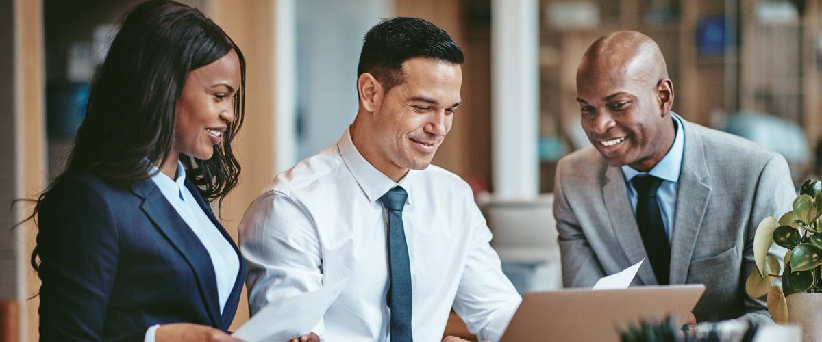 FSmiling group of diverse businesspeople going over paperwork together and working on a laptop at a table in an office