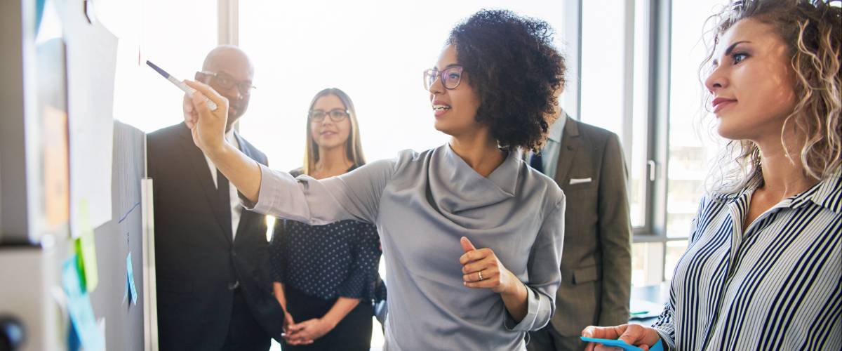 Diverse group of focused businesspeople brainstorming together on a whiteboard during a strategy session in a bright modern office