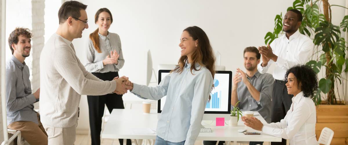 Boss shaking hand of employee congratulating, while business team applauding supporting colleague