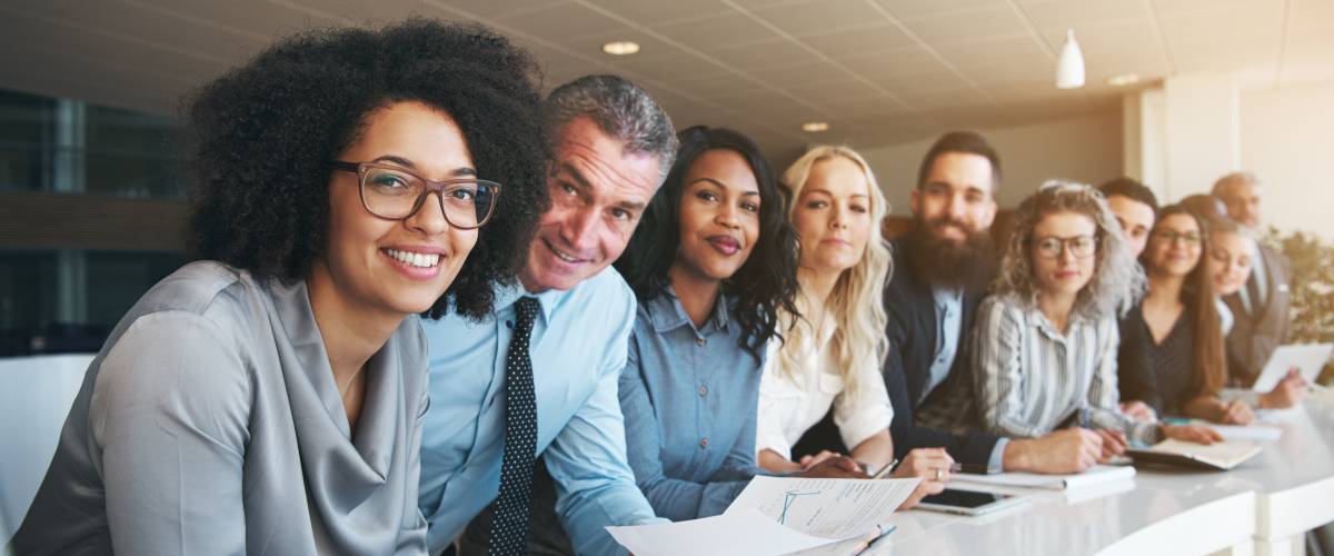 Portrait of a smiling group of diverse corporate colleagues standing in a row together at a table in a bright modern office
