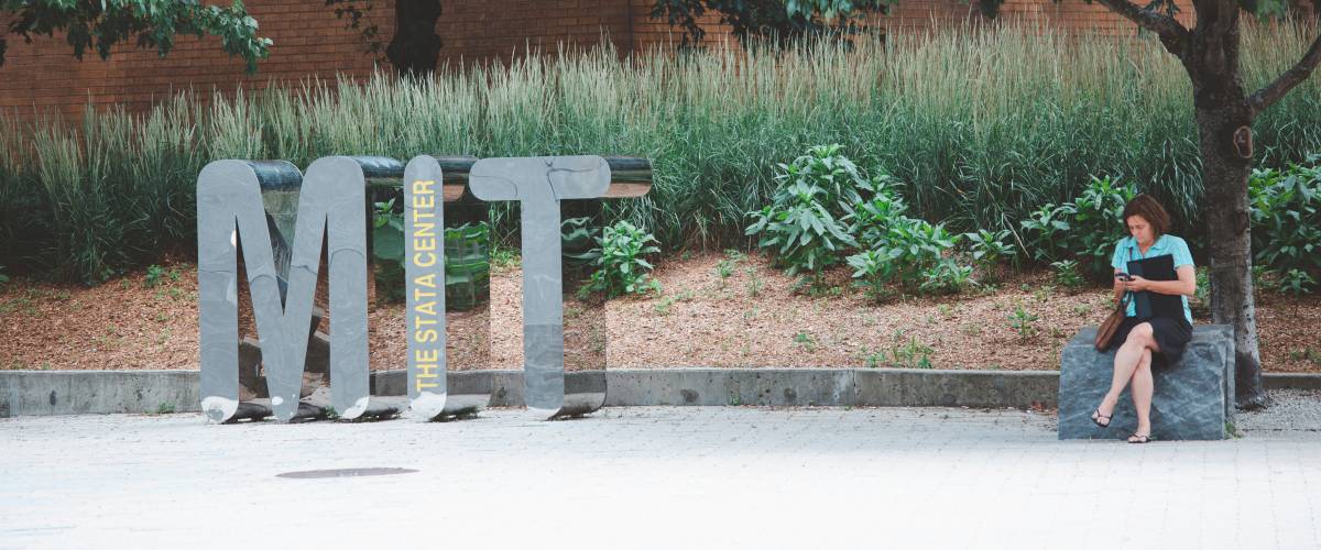 Student reads beside MIT sign on campus