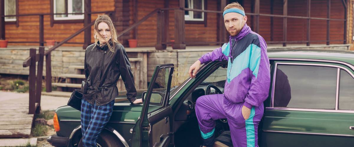 Guy and girl in clothes of the nineties, next to the old car
