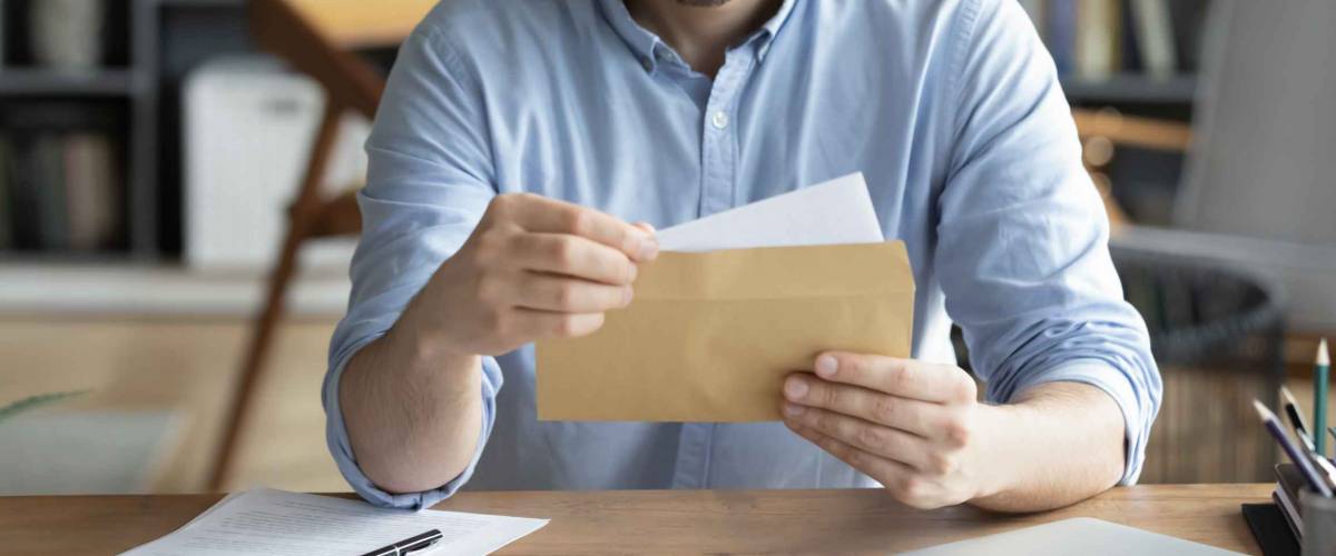 Serious businessman sit at workplace office desk holding envelope take out letter feels interested , received news on a work bonus