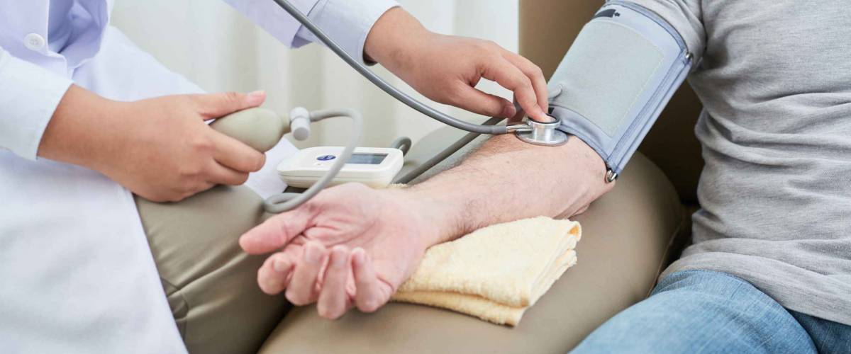 Crop shot of woman measuring blood pressure of senior man sitting in couch at home