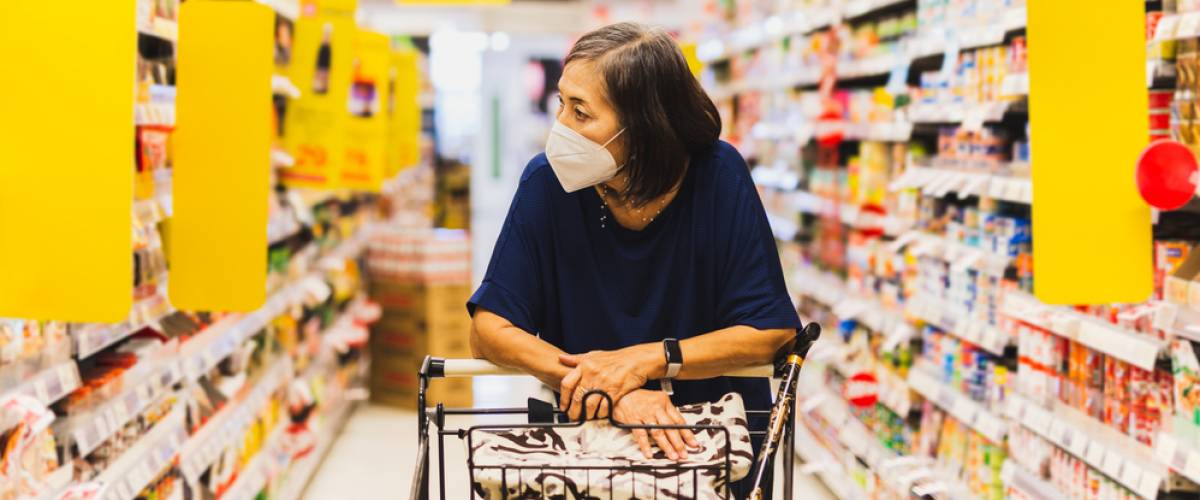A woman leaning on the grocery cart handle while she peruses the shelves