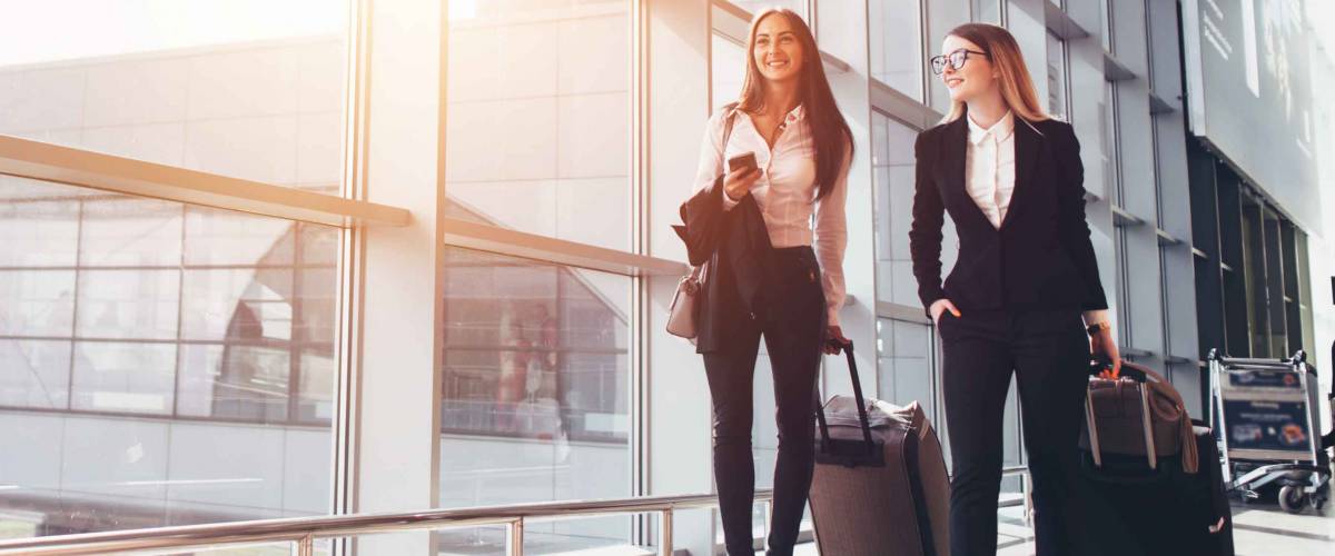Two smiling business partners going on business trip carrying suitcases while walking through airport passageway