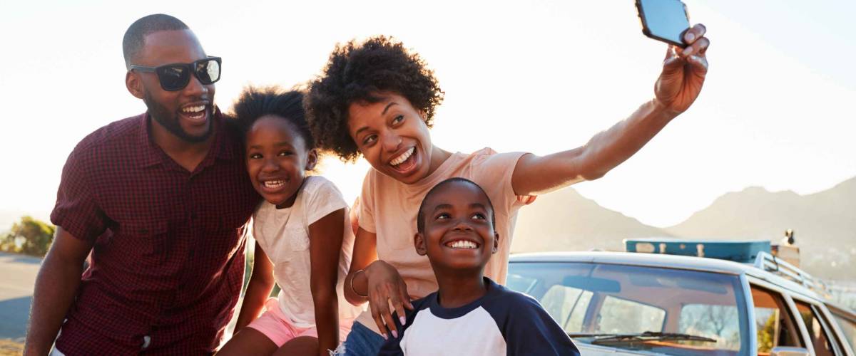 Family Posing For Selfie Next To Car Packed For Road Trip