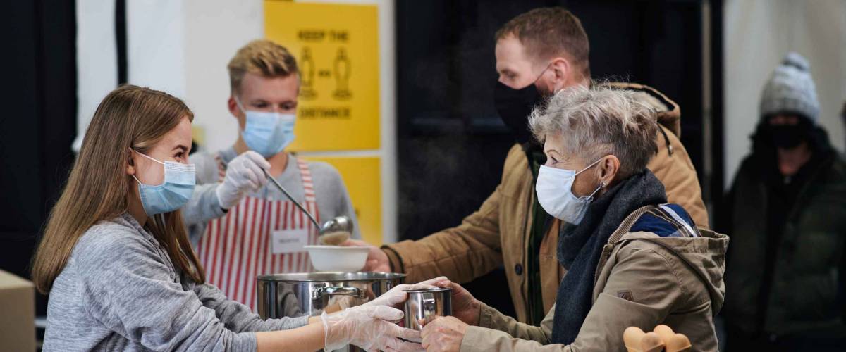 Volunteers serving hot soup for homeless in community charity donation center, coronavirus concept.