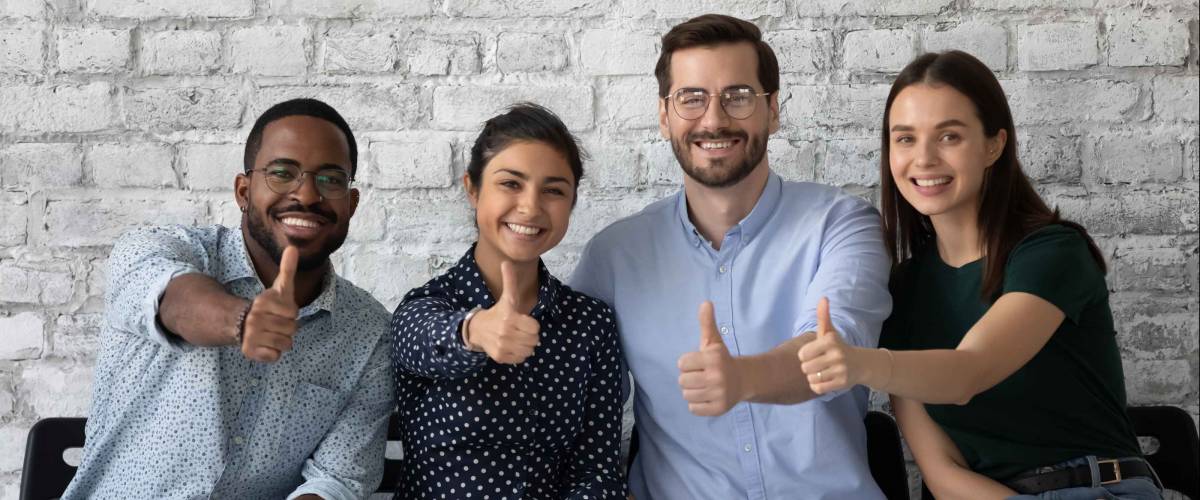 Portrait of four happy satisfied multiethnic persons sitting on row of chairs in office looking at camera showing thumbs up being hired