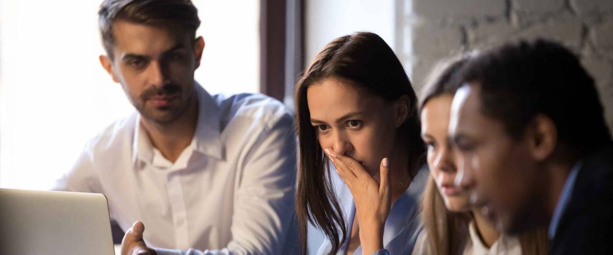 Group diverse surprised colleagues sitting at desk looking at computer screen looks shocked