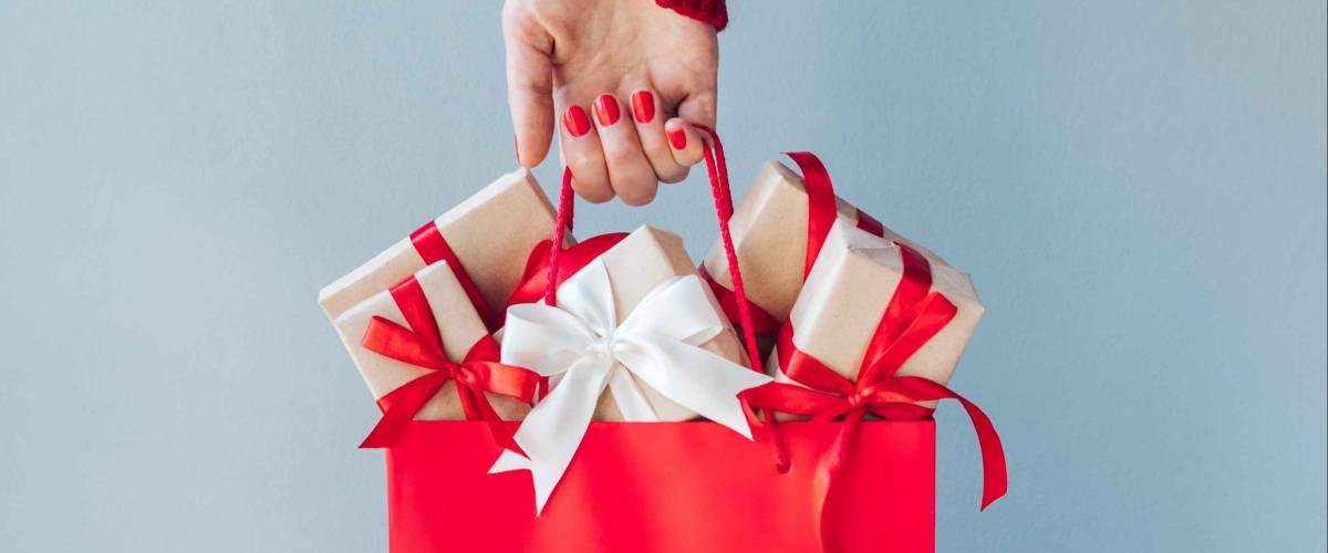 Cropped image of female hand with red polished nails holding shopping bag full of christmas gift boxes.
