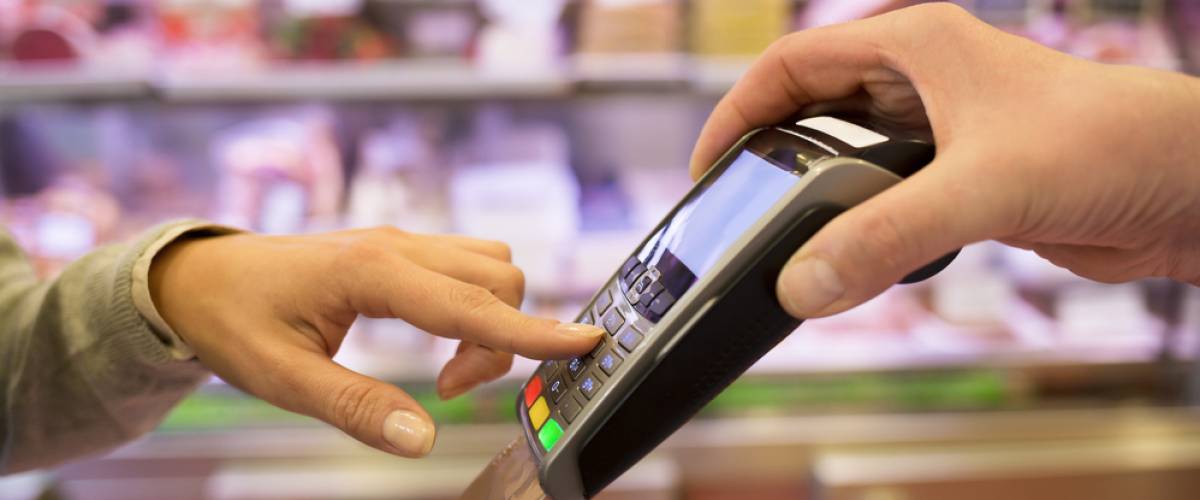 A person's hand enters numbers on a credit card scanner held by a store clerk