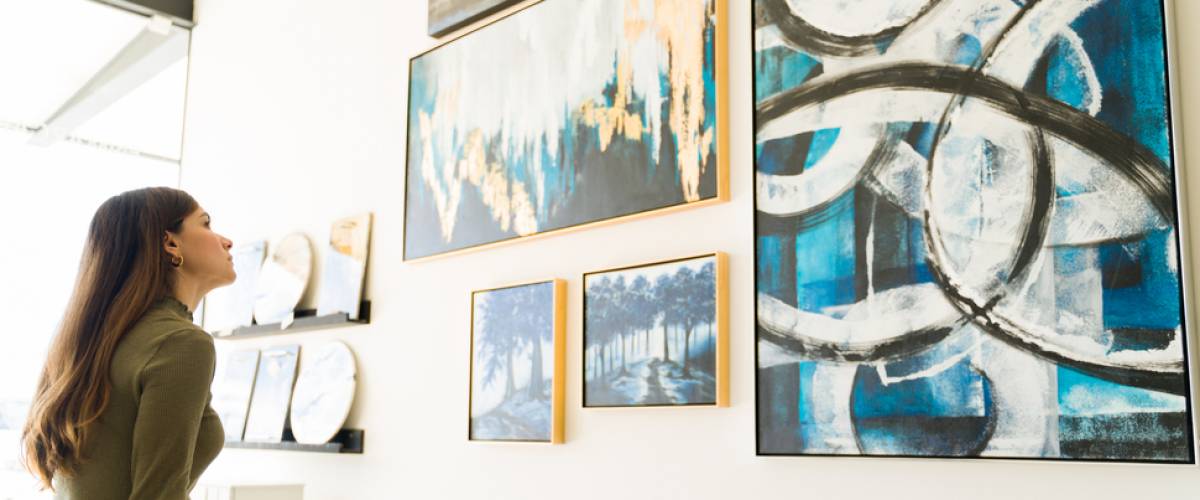 Side view of a beautiful young woman studying and watching the abstract paintings and colorful canvases during a visit to the art gallery