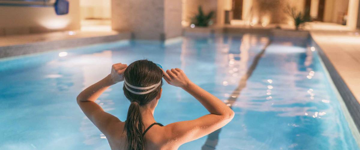 Woman getting ready to swim in indoor swimming pool at hotel or apartment building complex - condo amenities.