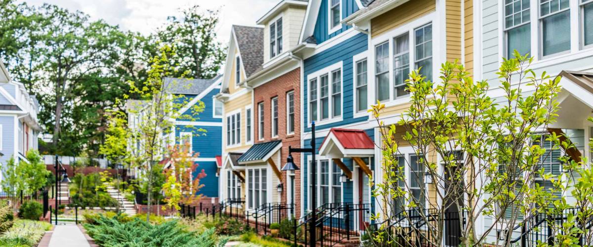 Row of colorful, red, yellow, blue, white, green painted residential townhouses, homes, houses with brick patio gardens in summer