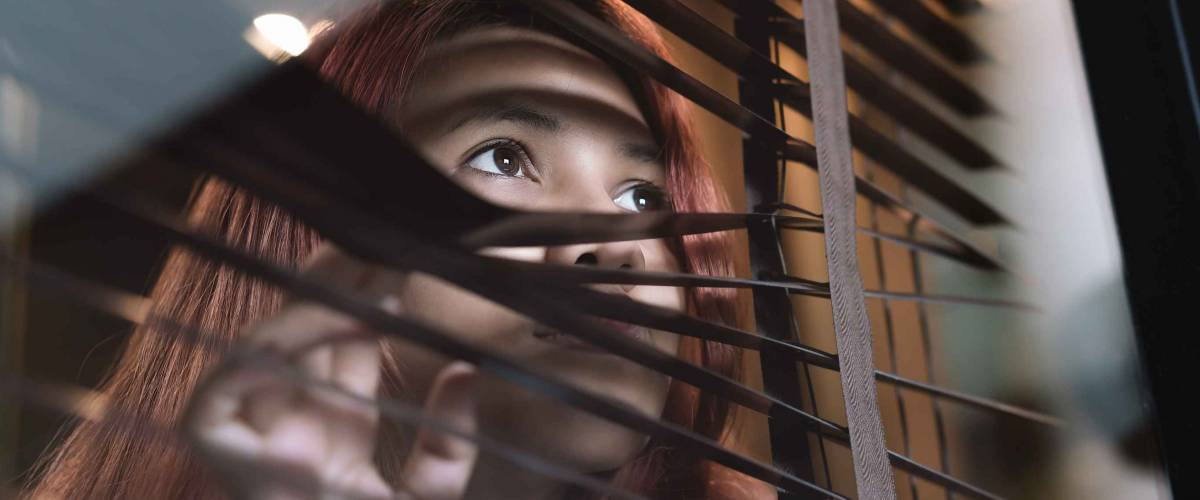 Asian woman looking through window blinds spying on neighbors
