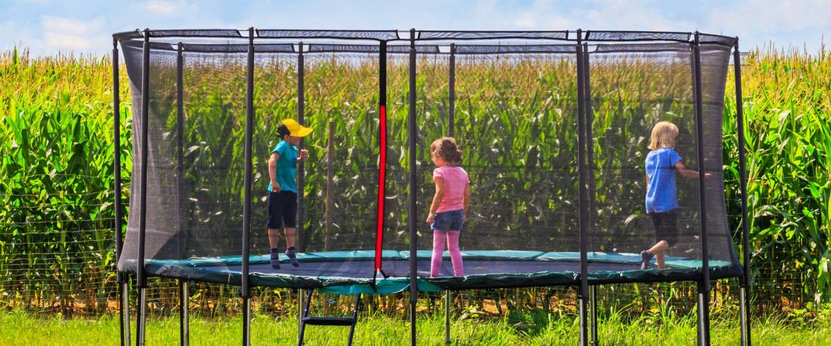 Children jump, run, trampolining in Open Jump Trampoline. Garden big Trampoline on the green grass near the corn field. Outdoor Trampoline with safety net with Zipper entrance.